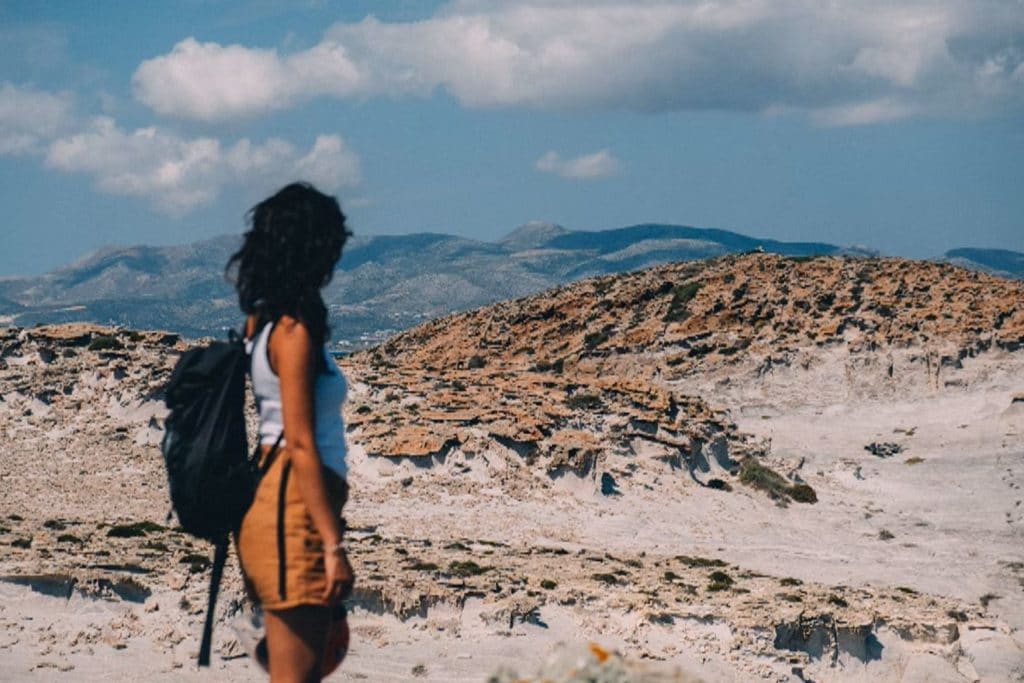 Viajar sozinha: mulher com uma mochila nas costas avistando uma paisagem nas montanhas.