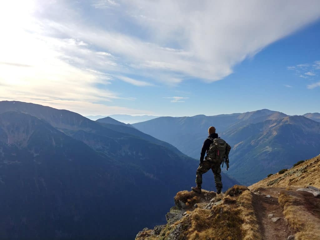 Foto da categorias "aventura": um homem está com uma mochila nas costas contemplando uma paisagem no alto de uma montanha.