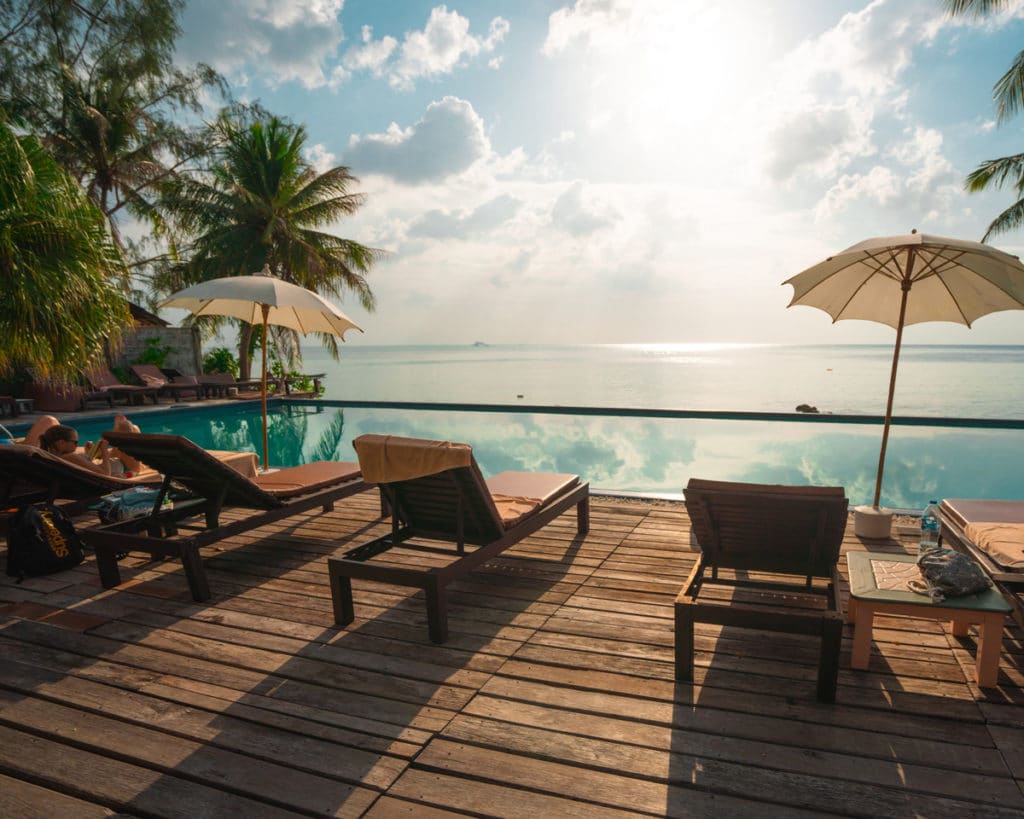 Foto da categorias "com hospedagem": deck com cadeiras de descanso e guarda-sol de frente para uma piscina.