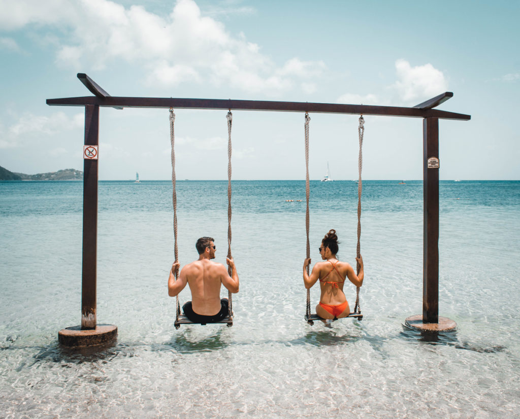 Foto da categoria "romance": um casal está sentado de costas em um balanço de madeira na beira do mar.