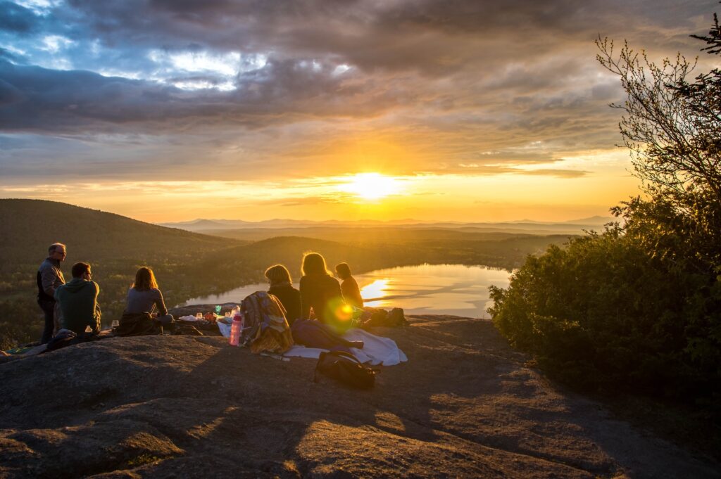 Imagem de um grupo de amigos contemplando o pôr-do-sol de uma montanha.